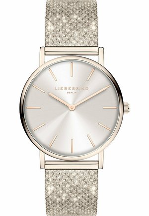 Montre ronde en argent avec un cadran à dégradé clair, des aiguilles dorées et un bracelet en maille argentée texturée. Marque "LIEBESKIND" affichée.