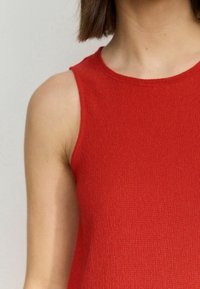 Rode geribde tanktop met een ronde hals, voorzien van een textuurstof. Mouwloos ontwerp benadrukt de schouders en het sleutelbeen.