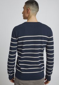 Marineblå stripete genser laget av mykt strikket stoff, med horisontale kremfargede striper, ribbede kantlinjer på hals og ermer, avslappet passform.