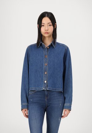 Veste en denim coupe courte bleu moyen, dotée d'un col classique, de boutons à l'avant et de longues manches avec des détails cousus.