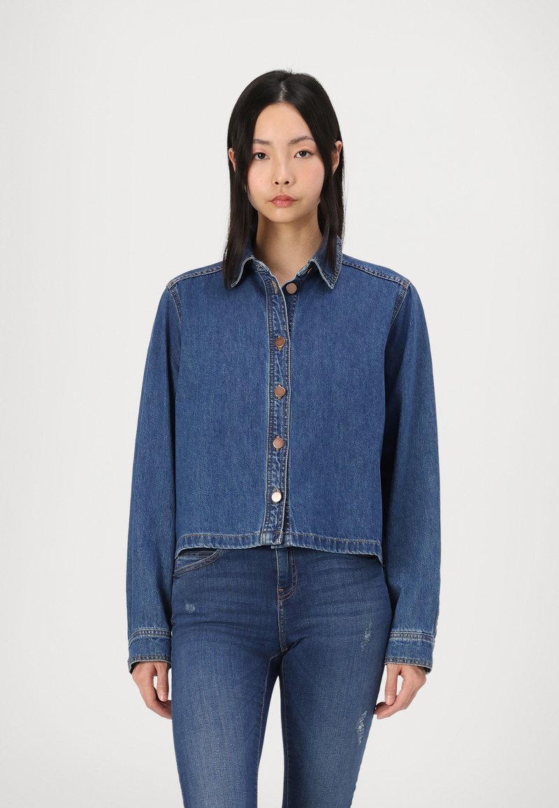 Kratka jeans jakna v srednje modri barvi, z klassičnim ovratnikom, sprednjimi gumbi in dolgimi rokavi z šivanimi detajli.
