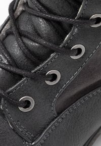 Sneaker in pelle nera con superficie testurizzata, occhielli in metallo e cuciture a contrasto. Presenta lacci neri e una silhouette curva.