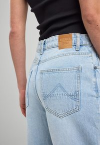 Light blue denim jeans with a high waist, featuring a leather label tagged "AMERICA TODAY" and distinct back pocket stitching.