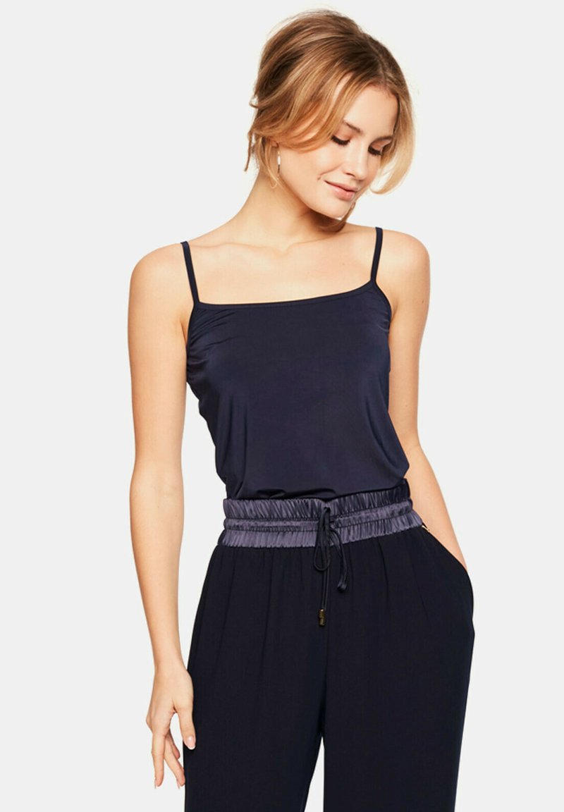 Granatowy top na ramiączkach z cienkimi paskami, z dopasowanym korpusem i elastycznym pasem z marszczeniami w kontrastowym odcienie, zestawiony z luźnymi czarnymi spodniami.