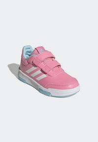 Zapatilla deportiva rosa con dos correas de velcro, tres rayas blancas, interior azul claro y suela blanca con detalles azules.