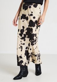 Jupe maxi en tissu beige avec un motif de taches noires. Présente une silhouette fluide et est assortie à des bottines noires.