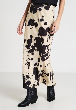Jupe maxi en tissu beige avec un motif de taches noires. Présente une silhouette fluide et est assortie à des bottines noires.