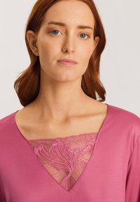 Rosa topp med V-ringning och spetsinlägg. Mjuk textur med en slät yta. Spetsen visar ett blommönster.