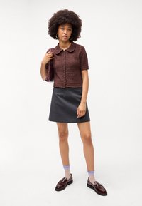 Καφέ υφασμάτινο πλεκτό κοντομάνικο σακάκι με γιακά Peter Pan, μαύρη φούστα Α γραμμής και παπούτσια από πατενταρισμένο δέρμα, συμπληρωμένα με κάλτσες με μπλε βούλες.