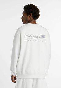 Felpa bianca dal taglio rilassato, con il logo grigio "New Balance Athletics" sul retro e dettagli a costine sui polsini e sull'orlo.