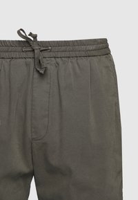 Spodnie z elastycznym pasem w ciemnoszarym kolorze; mają sznurek i boczną kieszeń; gładka tekstura, prosty fason i luźny krój.