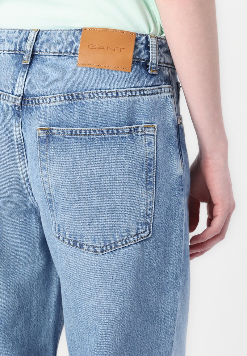 Lichtblauwe denim jeans met een leren GANT-label op de tailleband, voorzien van achterzakken met gestikte details en een klassieke pasvorm.