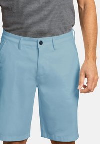 Pantalones cortos azul claro hechos de un tejido suave, con cierre de botón, pasadores para cinturón y bolsillos laterales, ofrecidos con una camisa de cuadros negra.