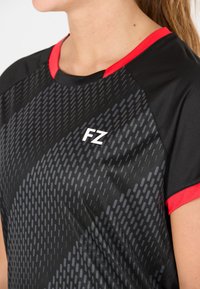 Musta urheilu paita punaisilla yksityiskohdilla, jossa on liukuvärjäyskuvio ja "FZ" logo. Valmistettu sileästä, hengittävästä kankaasta, jossa on lyhyet hihat.