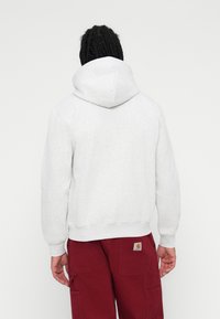 Felpa grigia con cappuccio dalla texture morbida, polsini a coste e orlo spaccato, abbinata a pantaloni bordeaux con logo a toppa.