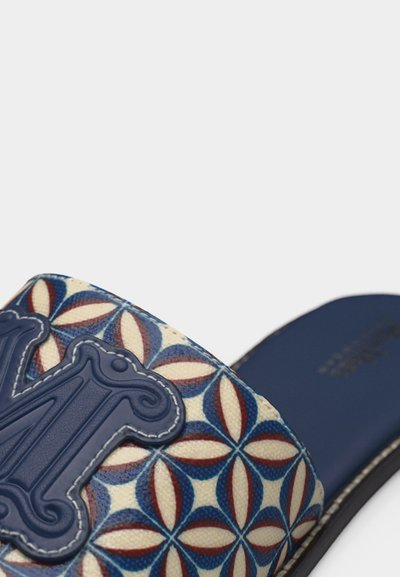 Σαγιονάρα με σχεδιασμένο λουράκι που διαθέτει γεωμετρικό σχέδιο σε μπλε, κόκκινο και κρεμ αποχρώσεις, με κεντημένο διακοσμητικό έμβλημα σε ναυτικό μπλε.