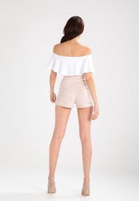 Haut blanc à épaules dénudées avec bordure à volants, associé à un short beige taille haute. Mannequin portant des talons nus, vu de dos.