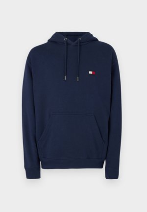 Marineblauer Kapuzenpullover mit vorderer Kängurutasche, Kordelzug in der Kapuze, gerippten Bündchen und kleinem rechteckigem Logo-Patch auf der Brust.