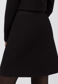 Svart stickad kjol med en utsvängd A-linjeform, med en slät yta och ett enfärgat mönster. Längd till mitten av låret med minimal sömdetalj.