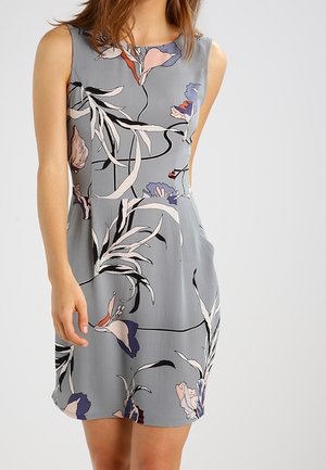 Robe grise sans manches avec de grands motifs floraux abstraits en noir, blanc, violet et rose, portée par une personne devant un fond clair uni.