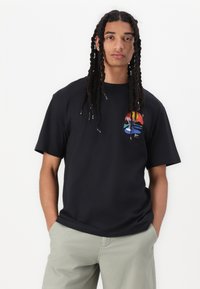 Sort bomulds T-shirt med korte ærmer, der har et flerfarvet grafisk design af en sol og vandbølger på venstre brystområde.