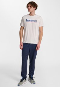 Vit t-shirt med kort ärm och "hummel" grafik; marinblå sweatpants; sportskor med grå och blå accenter, texturerat tyg.