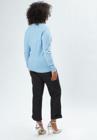 Helles blaues, langärmliges Sweatshirt mit geripptem Saum und Bündchen, kombiniert mit schwarzen, hochgekrempelten Hosen und silbernen High Heels.