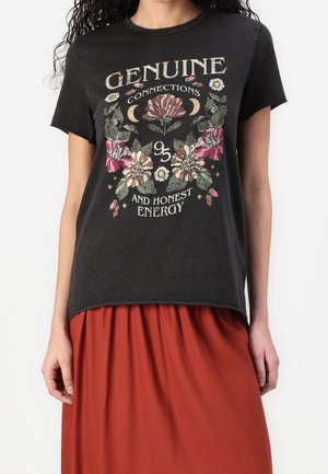 Musta t-paita, jossa on kukkakuosi ja teksti "Aitoja yhteyksiä 95 ja rehellistä energiaa", yhdistetty ruosteenväriseen hameeseen.