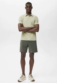Polo shirt vert clair associé à un short vert foncé, arborant une coupe classique. Le modèle porte des baskets beiges avec des semelles texturées.