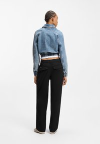 Κοντό τζιν μπουφάν με ανοιχτό μπλε πλύσιμο, ελαστική μέση και μακριά μανίκια, συνδυασμένο με μαύρο παντελόνι φαρδύ στο πόδι με τσέπες στο πίσω μέρος.