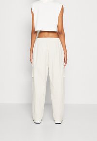 Lehké krémové cargo kalhoty s elastickým pasem, bočními kapsami a volným střihem. Kombinované s bílým krátkým topem bez rukávů.