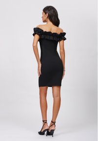 Black off-shoulder dress with ruffled trim, fitted design, mid-thigh length, and smooth texture. Worn with strappy black heels.