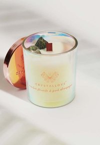 Świeca zapachowa w przezroczystym, iryzującym szklanym pojemniku z różowym metalowym wieczkiem, ozdobiona kamieniami szlachetnymi oraz drewnianym knotem.