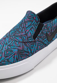 Teniska na nazouvání s černým, růžovým a modrým geometrickým vzorem. Na boku je černé logo Nike a bílá gumová podrážka.