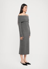 Siva pletena obleka z off-shoulder designom, dolgimi rokavi, oprijetim krojem in dolžino do polovice meč, v kombinaciji z črnimi pointed flats.