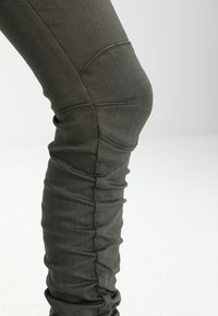 Mörkgröna, stretchiga byxor med slim fit, med framträdande sömmar och en strukturerad yta som samlar sig något vid knäna.