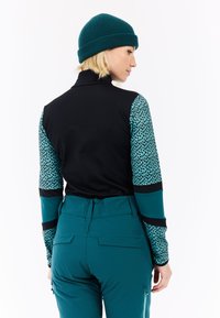 Teal en zwarte actieve kledingtopp met een patroon op de mouwen, gecombineerd met teal broek. Materiaal lijkt rekbaar en aansluitend.