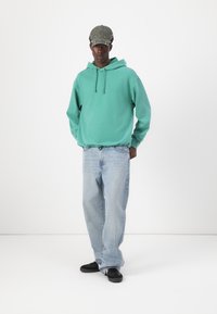 Hanorac turquoise cu sireturi, blugi denim light blue și adidași negri. Căciula este verde măslin cu un tiv cusut.