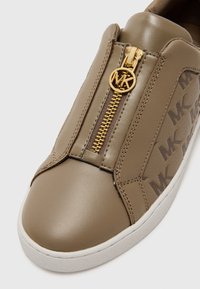 Béžové kožené slip-on tenisky so zlatým zipsom a MK logom. Disponujú hladkým povrchom a bielou gumovou podrážkou s jemným brandingom.