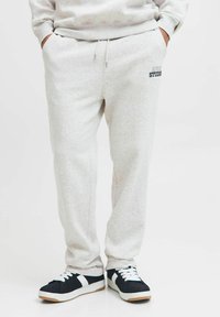 Lys grå sweatpants lavet af blødt stof, med snøre i taljen og et lille logo på venstre side. Sammen med sorte og hvide sneakers.