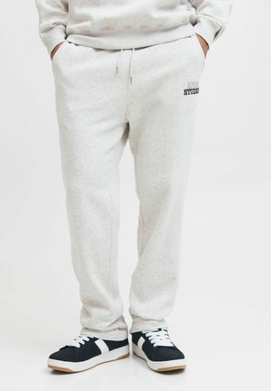 Light grey sweatpants made of soft fabric, featuring a drawstring waist and a small logo on the left side. Paired with black and white sneakers.