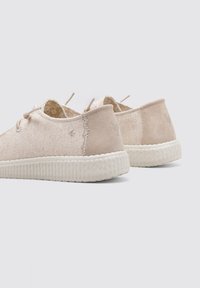 Zapatos de ante beige con un acabado texturizado, diseño de cordones y suela de goma blanca contrastante con un patrón estriado y detalle de logo.