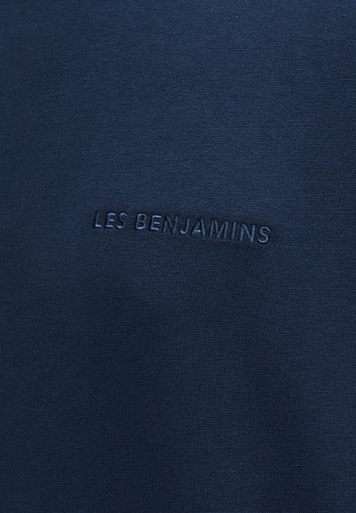 Υφασμα σε ναυτικό μπλε με κέντημα "LES BENJAMINS" σε νήμα ίδιο με το ύφασμα στο κέντρο, παρουσιάζοντας λεπτές υφές και λεπτομέρειες ραφής.