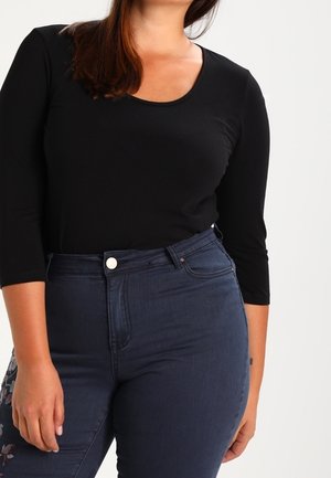 Czarna bluzka z długim rękawem i okrągłym dekoltem w połączeniu z granatowymi jeansami z wysokim stanem, ozdobionymi kwiatową haftą na lewej udzie.