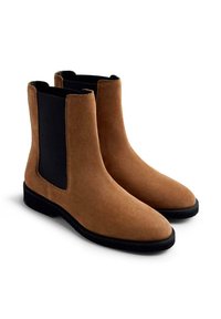 Botines Chelsea de ante marrón con paneles elásticos laterales negros y punta redonda. La suela es negra y texturizada para un mejor agarre y estabilidad.