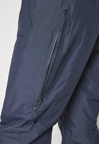 Μπλε ναυτικού χρώματος παντελόνια εξωτερικού χώρου με λεία υφή και τσέπη στο πλάι με φερμουάρ; διαθέτουν ενισχυμένα ραψίματα και ρυθμιζόμενο κορδόνι στη μέση.