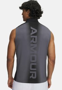 Bezramienna koszulka sportowa w ciemnoszarym kolorze z czarnym tyłem, z pionowym logo "ARMOUR" w kontrastującym odcieniu szarości, wykonana z gładkiego, lekkiego materiału.