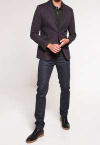 Tmavý blazer, zelená polo tričko, úzké tmavé džíny a černé šněrovací boty. Blazer má jedno knoflíkové zapínání a dvě přední kapsy. Oblečení je pohodlné, ale přesto rafinované.