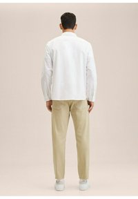 Miesten asu, jossa on valkoinen napillinen paita ja vaaleanbeiget kapeat housut, valkoiset lenkkarit; sileä kangas ja kaksi takataskua housuissa.