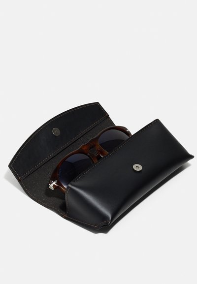 Black leather sunglasses case with a smooth finish, featuring a metal snap closure and brown stitching, partially open to reveal brown-framed sunglasses.